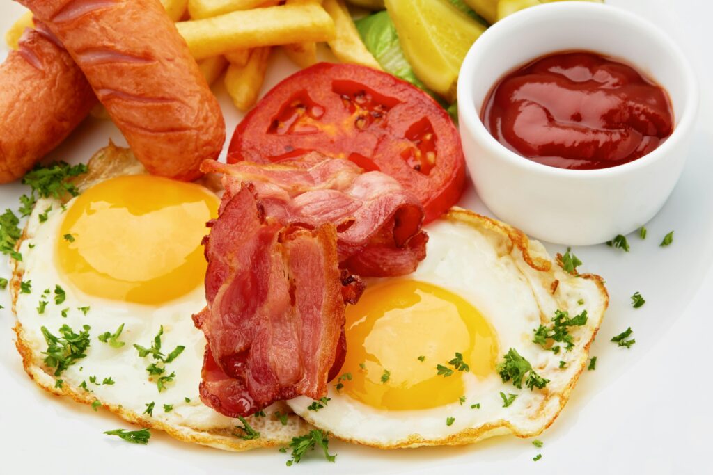 Tasty full breakfast with eggs, bacon, sausages, and fresh vegetables.