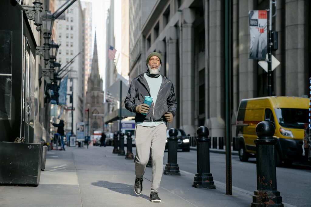 Senior man wearing activewear carrying a water bottle while walking in a bustling city street.