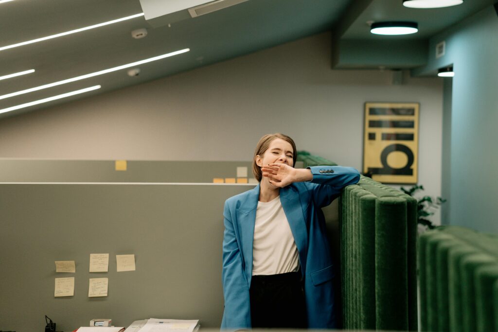 Exhausted woman in blue blazer yawning during workday in corporate office.